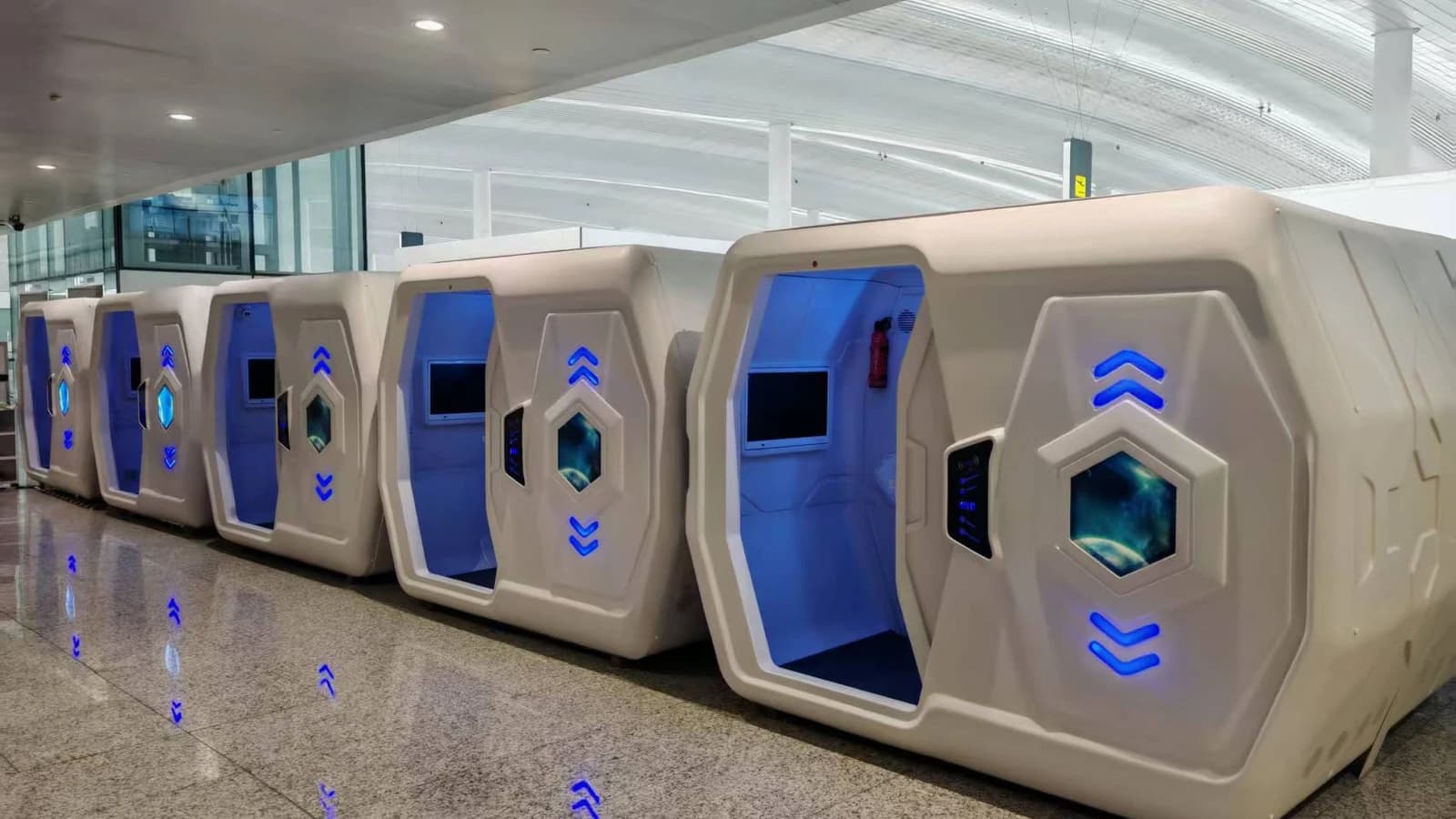 Row of single white capsule beds with blue interior lighting in an airport terminal