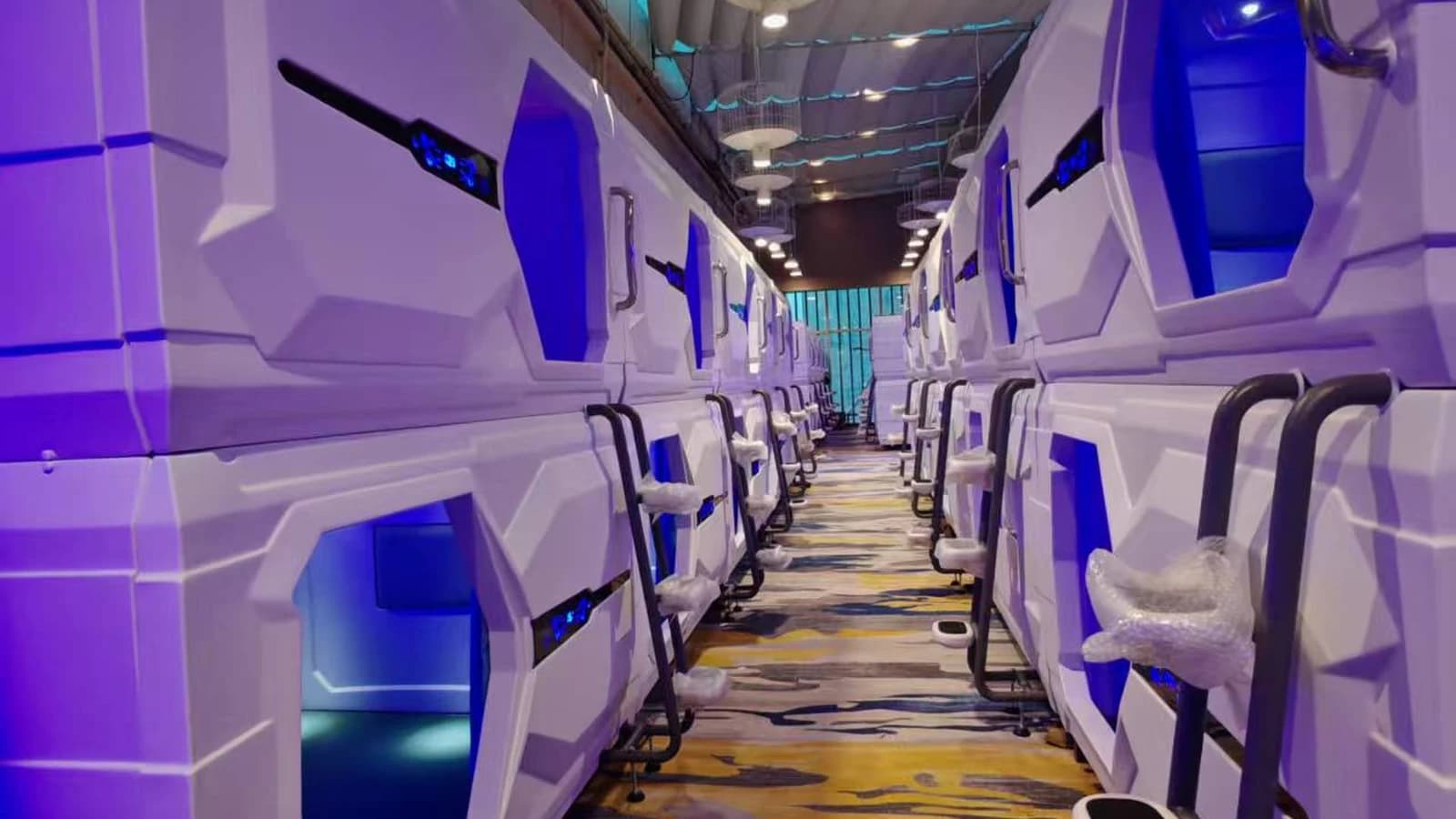 Aisle between two rows of double-deck white capsule beds in a finished capsule hotel