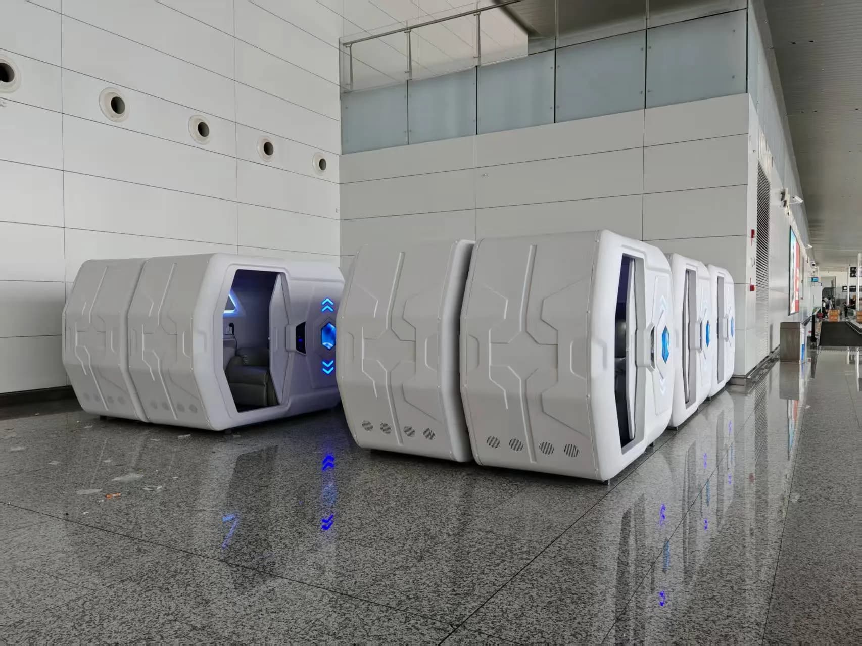 Row of standalone white sleep pods installed at floor level in an airport terminal